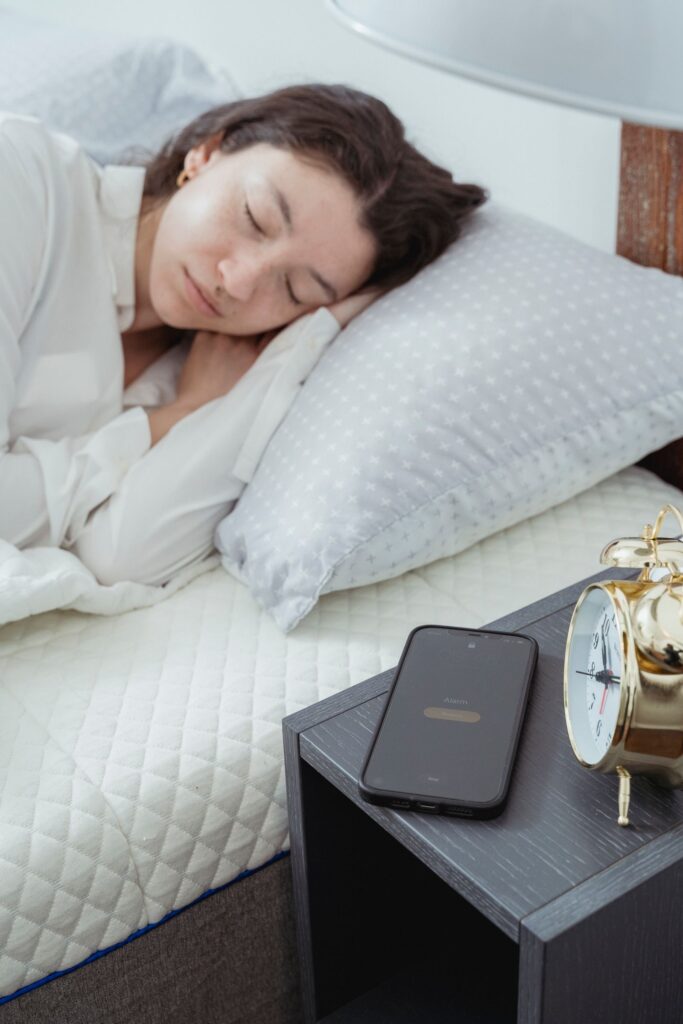 Kvinde sover med vækkeur og mobiltelefon ved sengen